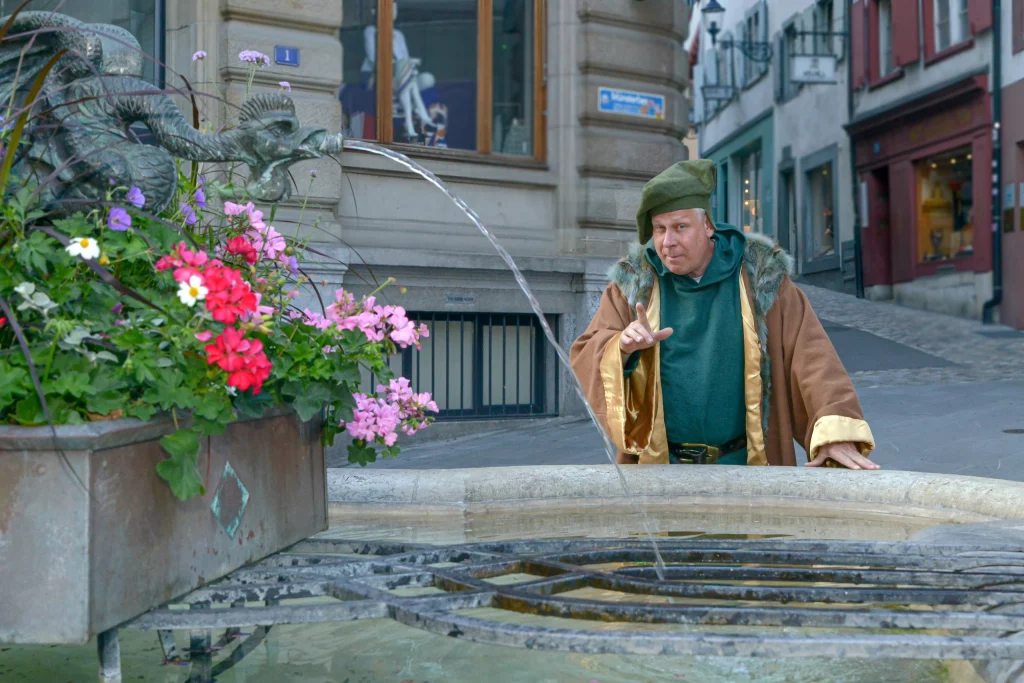 Wigand Neumann in der Rolle des Erasmus von Rotterdam bei einer schauspielerischen Stadtfuehrung in der Altstadt von Basel vor einem Brunnen